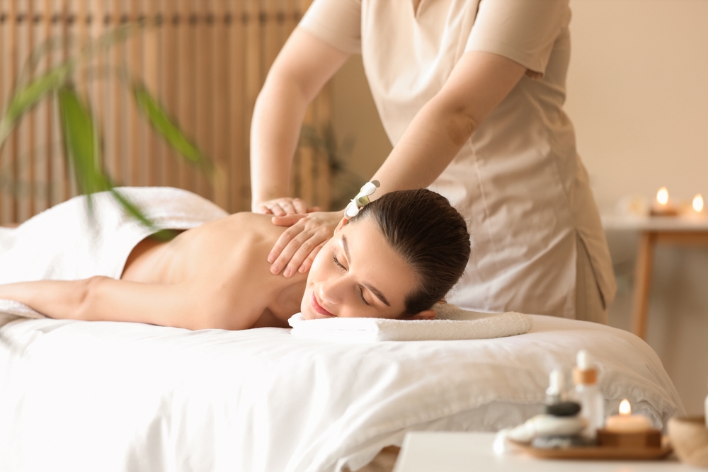 Spa therapist performing relaxing shoulder and neck massage on client lying on white bed in serene wellness setting